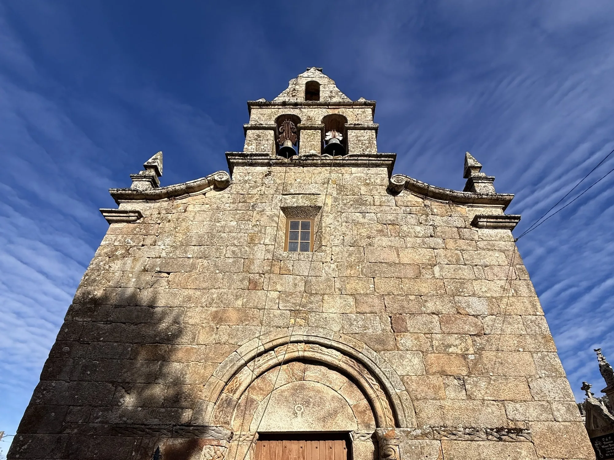 Fachada de pedra da igrexa de San Cibrao de Nocedo: a espadana barroca coas dúas campás e, debaixo, o arco da portada románica