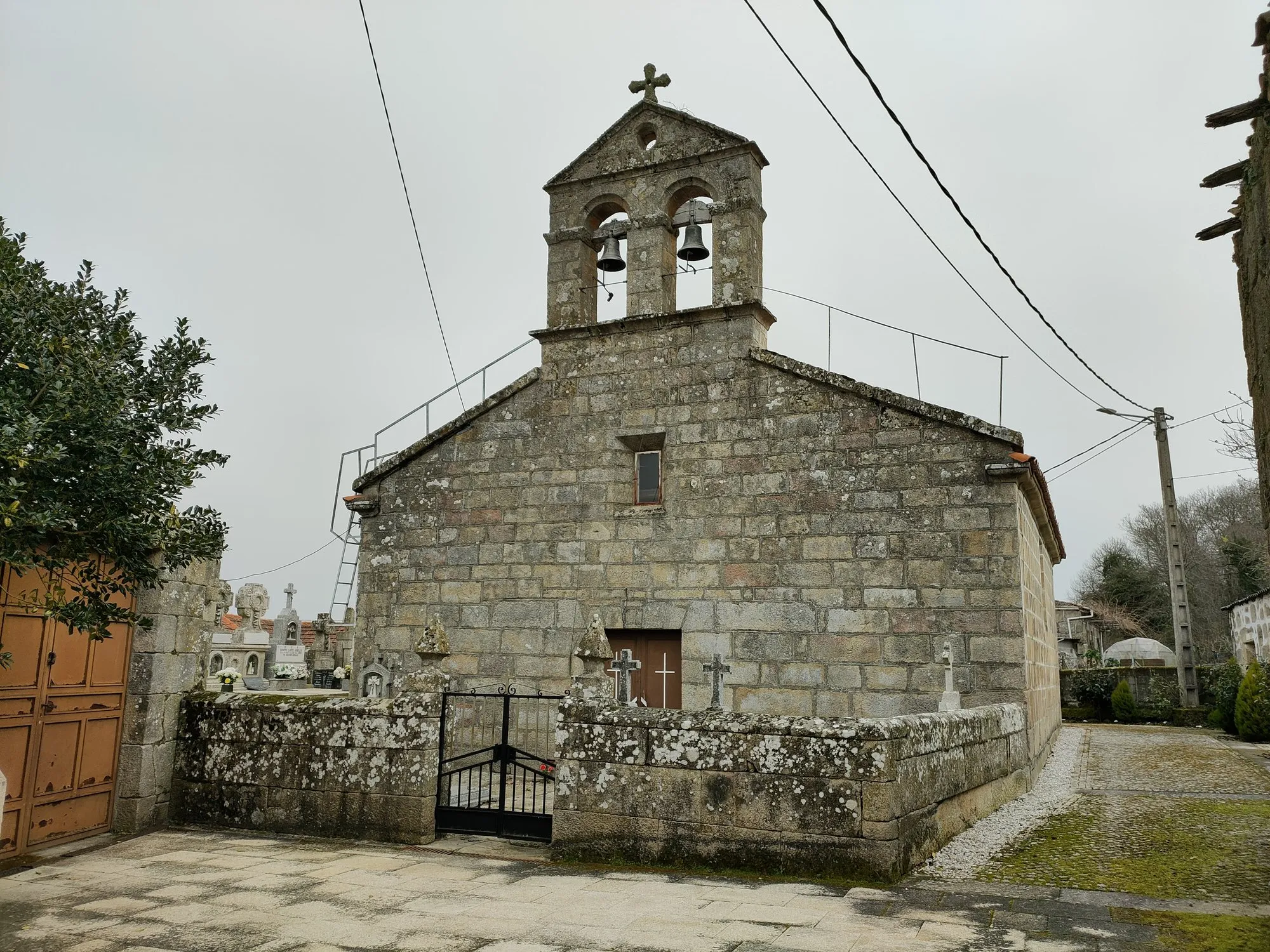 A igrexa parroquial de Mosteiro de Ribeira hoxe: pedra de granito, espadana con dúas campás e o adro co cemiterio, nun día de néboa