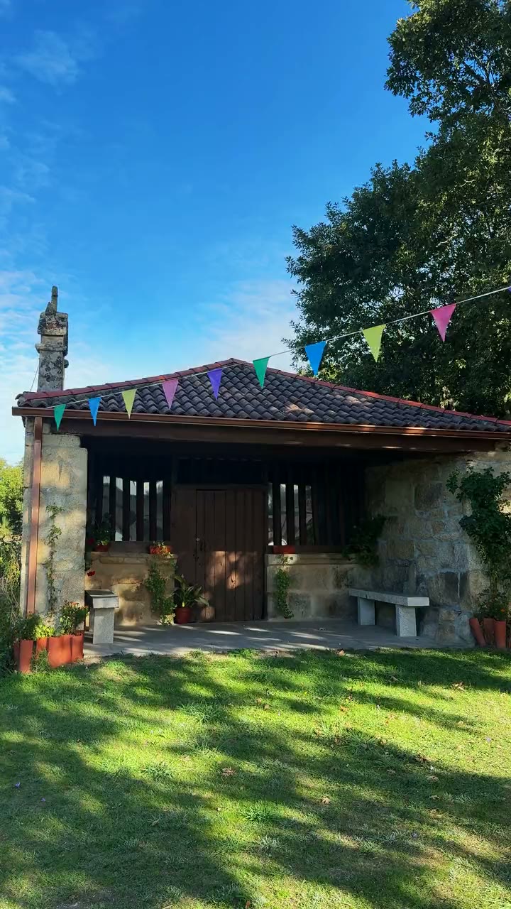 A capela da Nosa Señora da Asunción das Fontelas coas bandeiriñas da festa, o seu cruceiro baixo un carballo e o manancial ao pé dunha rocha con musgo